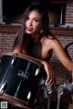 A woman in a black dress sitting next to a drum set.