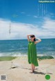 A woman in a green dress standing on a rock by the ocean.