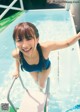 A woman in a blue bathing suit standing next to a swimming pool.