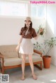 a woman standing in front of a couch wearing a brown shirt and skirt