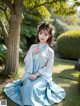 A woman in a blue hanbok sitting under a tree.