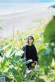 A woman standing in a field of tall grass next to the ocean.