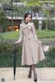 A woman in a beige trench coat holding an umbrella.