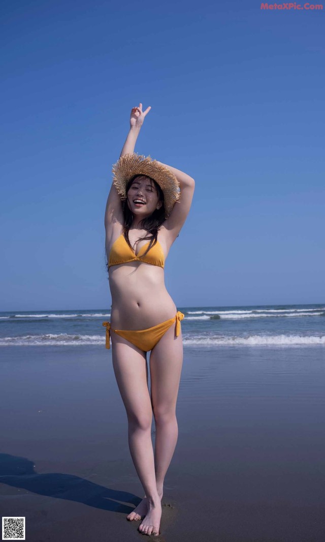 A woman in a yellow bikini and straw hat on the beach.