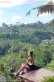 A woman sitting on a wooden platform in the middle of a lush green forest.