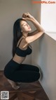 A woman in a black sports bra top and black leggings leaning against a wall.