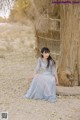 A woman in a blue dress sitting next to a tree.