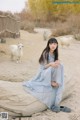 A woman sitting on a log in front of a herd of goats.