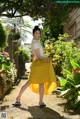 A woman in a yellow skirt is walking through a garden.