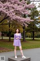 A woman in a purple dress standing in front of a tree.