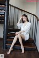 A woman sitting on a wooden staircase in a white dress.