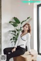 a woman sitting on top of a wooden bench next to a plant