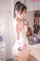 A woman in a white dress is standing in a kitchen.