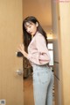 A woman in a pink shirt and jeans leaning against a door.
