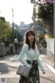 A woman in a green sweater and floral skirt is walking down the street.