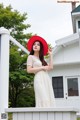 A woman in a white dress and red hat standing on a porch.