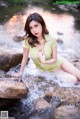 A woman in a green dress sitting on a rock in a stream.