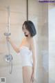 A woman in a white bathing suit standing in a shower.