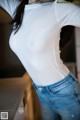 A woman in a white shirt and blue jeans standing in a kitchen.