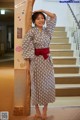 A woman in a kimono leaning against a brick wall.