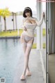 A woman in a white sweater and stockings posing by a pool.