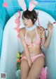 A woman in a pink bunny costume sitting in a bathtub.